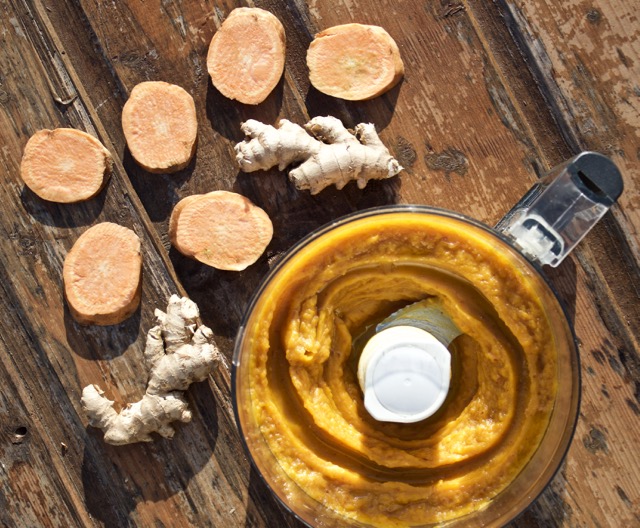 sweet potato mash in a food processor, with slices of sweet potato and whole ginger on a wood background